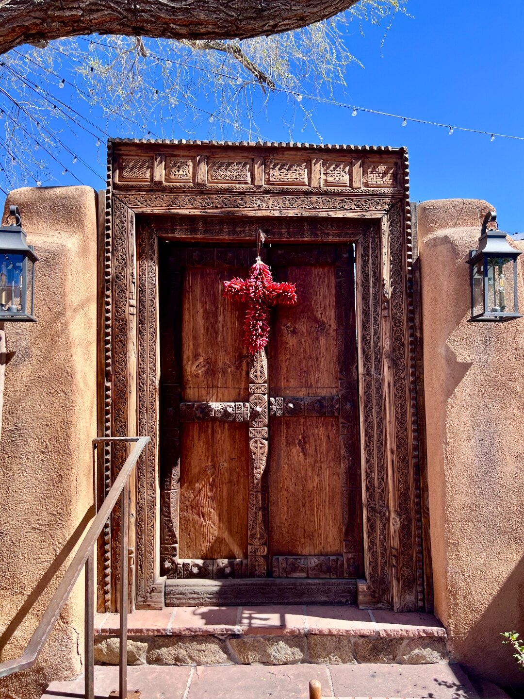 Carved wooden doorway with a red cross of chiles, suggesting welcome and threshold